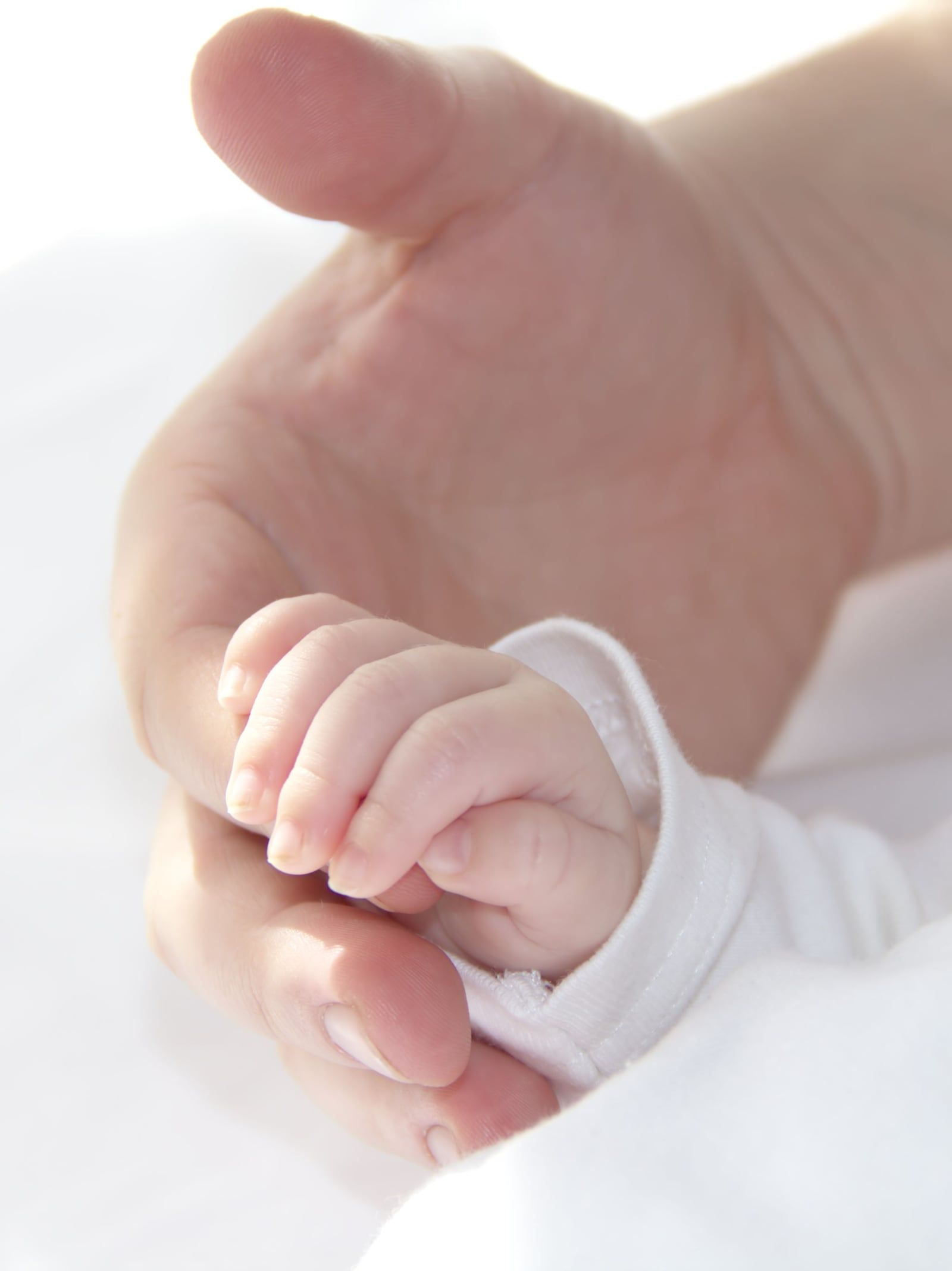 Babyhand umfasst den Finger eines Erwachsenen.